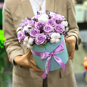 Композиция в шляпной коробке из лиловых роз Меритим, гипсофил и хлопка в Павловском Посаде